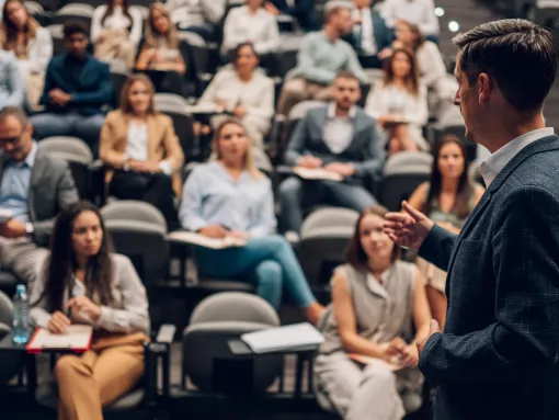 Speaker presenting to a large group of people attending a seminar, learning and taking notes in a lecture hall